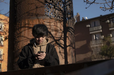 Asian teenage boy looking at mobile phone on street. madrid. spain