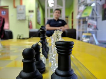 Close-up of chess pieces on table with man sitting in background