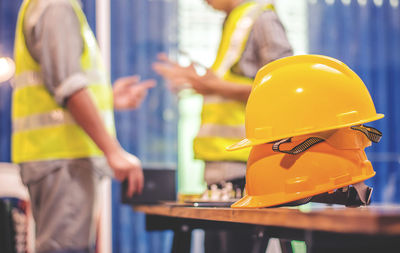 Close-up of hardhats on table with construction workers standing in background