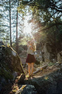 Rear view of young woman standing on rock in forest