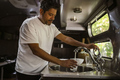 Man filling drinking water through faucet in camper trailer