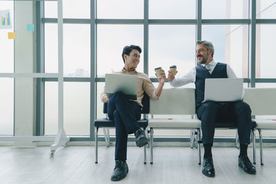 Full length of smiling businessman holding coffee cup at office