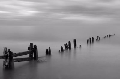 Wooden posts in sea against sky