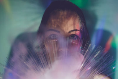 Close-up portrait of young woman holding fiber optic with smoke