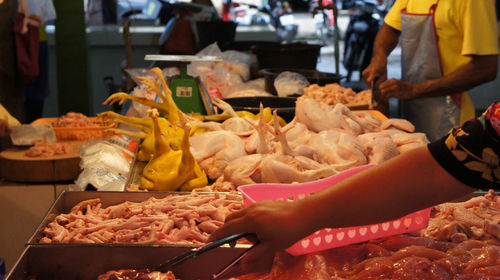 Cropped hand of woman picking meat with tongs in market