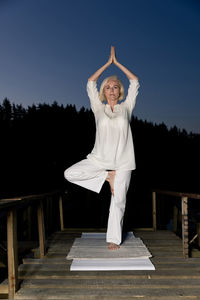 Middle aged woman doing yoga outdoors in forest