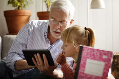 Grandfather showing tablet computer to granddaughter while studying at home