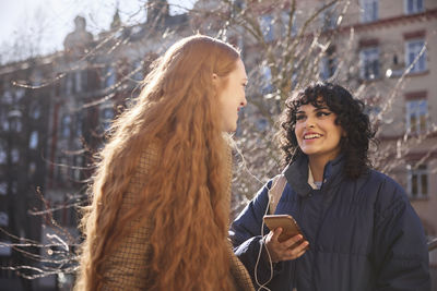 Female friends listen to music or podcast while sharing in-ear headphones