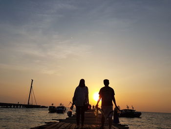 Silhouette man and woman on pier by sea against sky during sunset