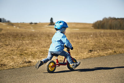 Boy with cycling helmet riding balance bicycle on road