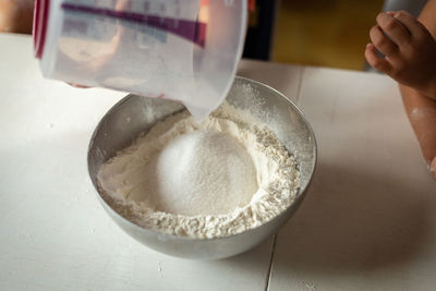 A close view of the hand of the child adding sugar to flour