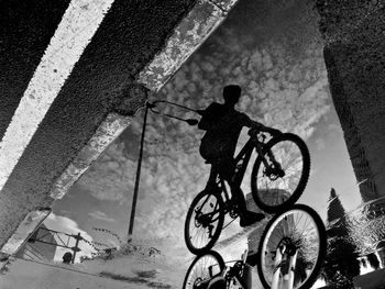 Reflection of man riding bicycle on puddle at street