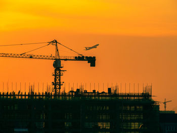 Silhouette of tower cranes in operation at construction site with during sunset. 