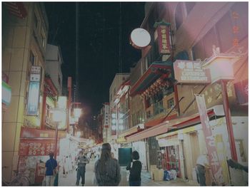 People walking on illuminated street in city at night