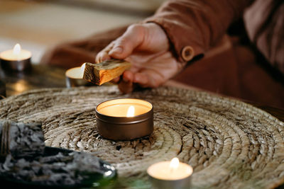 Woman hands burning palo santo, before ritual on the table with candles and green plants. smoke of