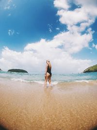 Side view of seductive woman standing on shore at beach against sky