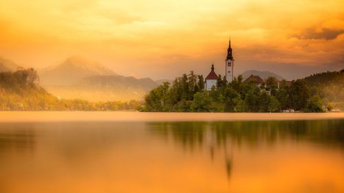 Scenic view of lake and buildings against sky during sunset