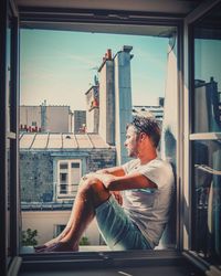 Man sitting on window sill in city