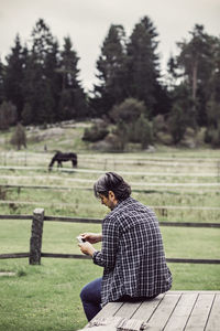 Rear view of male farmer using mobile phone on porch at organic farm