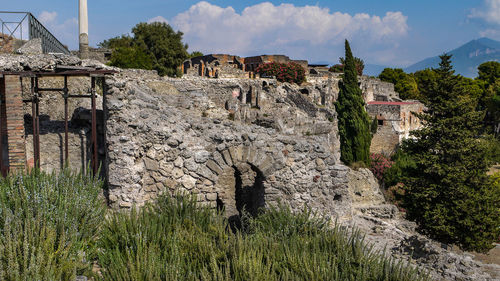 Stone wall by trees and houses against sky