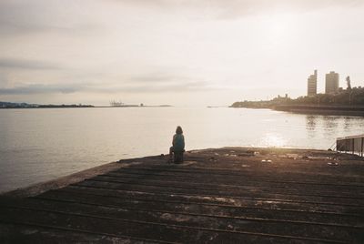 Rear view of man sitting on pier at sea against sky