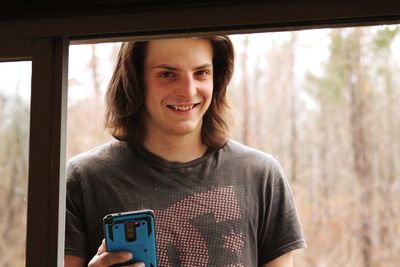 Close-up portrait of smiling young man looking through window