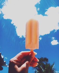 Close-up of hand holding ice cream against sky