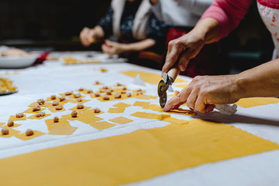 Unrecognizable crop aged female cutting dough with wheel cutter while cooking tasty traditional tortellini on table in kitchen