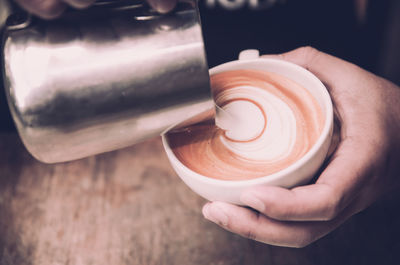 Cropped hands of woman pouring milk in coffee