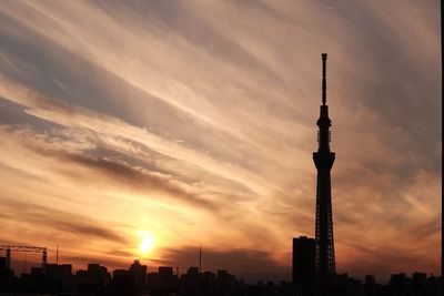 Silhouette of city against cloudy sky during sunset