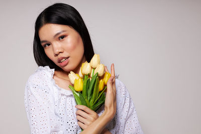Portrait of young woman holding yellow flower against white background
