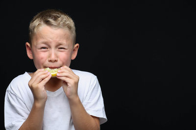 Portrait of boy eating food against black background