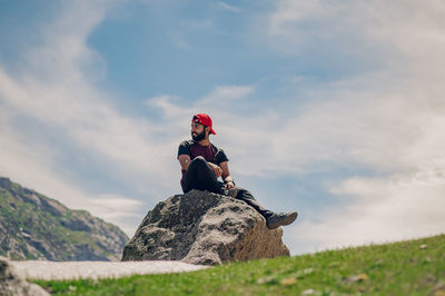Low angle view of man sitting on rock against sky