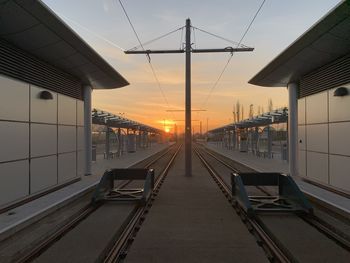 Railroad station platform against sky during sunset