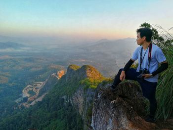 Young woman sitting on rock against sky