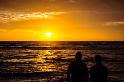 Rear view of silhouette man standing at beach during sunset