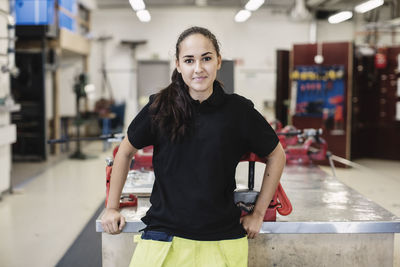 Portrait of smiling female auto mechanic student standing in workshop