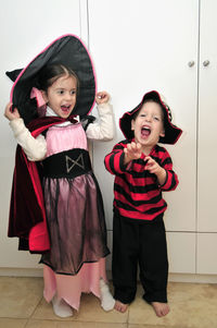 Full length of cheerful siblings wearing halloween costumes standing at home