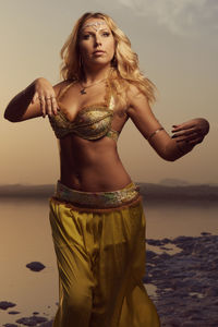 Portrait of beautiful woman standing at beach during sunset