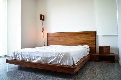 Bed base, bedroom with mat on the floor, clay pot in the background, wooden credenza and mirror.