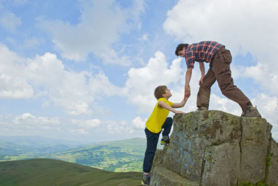 Teenage boy helping friend to climb rock