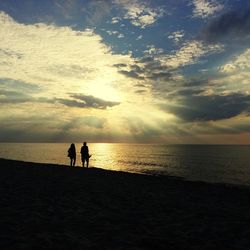 Silhouette people on beach against sky during sunset