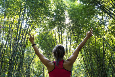 Rear view of woman with arms raised standing in forest