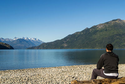 Rear view of man sitting on mountain against clear sky