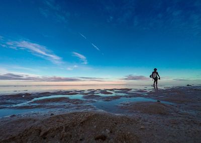 Man walking on beach against blue sky