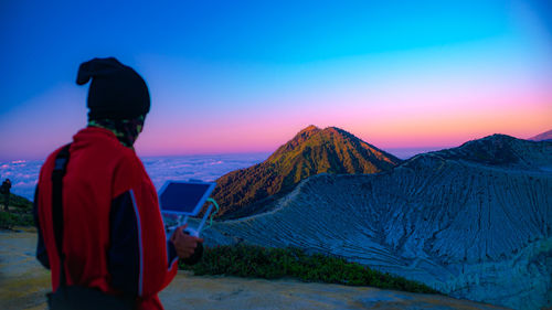 Rear view of man on mountains against sky during sunset