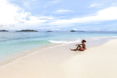 Man sitting on beach against sky