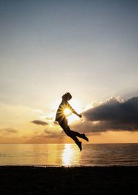 Silhouette man jumping on beach against sky during sunset