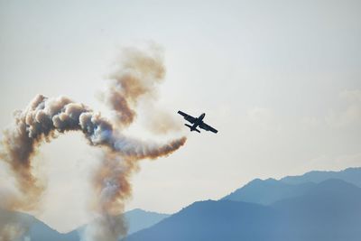 Low angle view of airplane emitting smoke while flying in sky