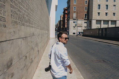 Portrait of young man standing against wall in city